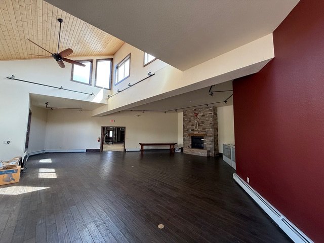 Large open gallery room with high wood ceiling, tall windows and a stone fireplace